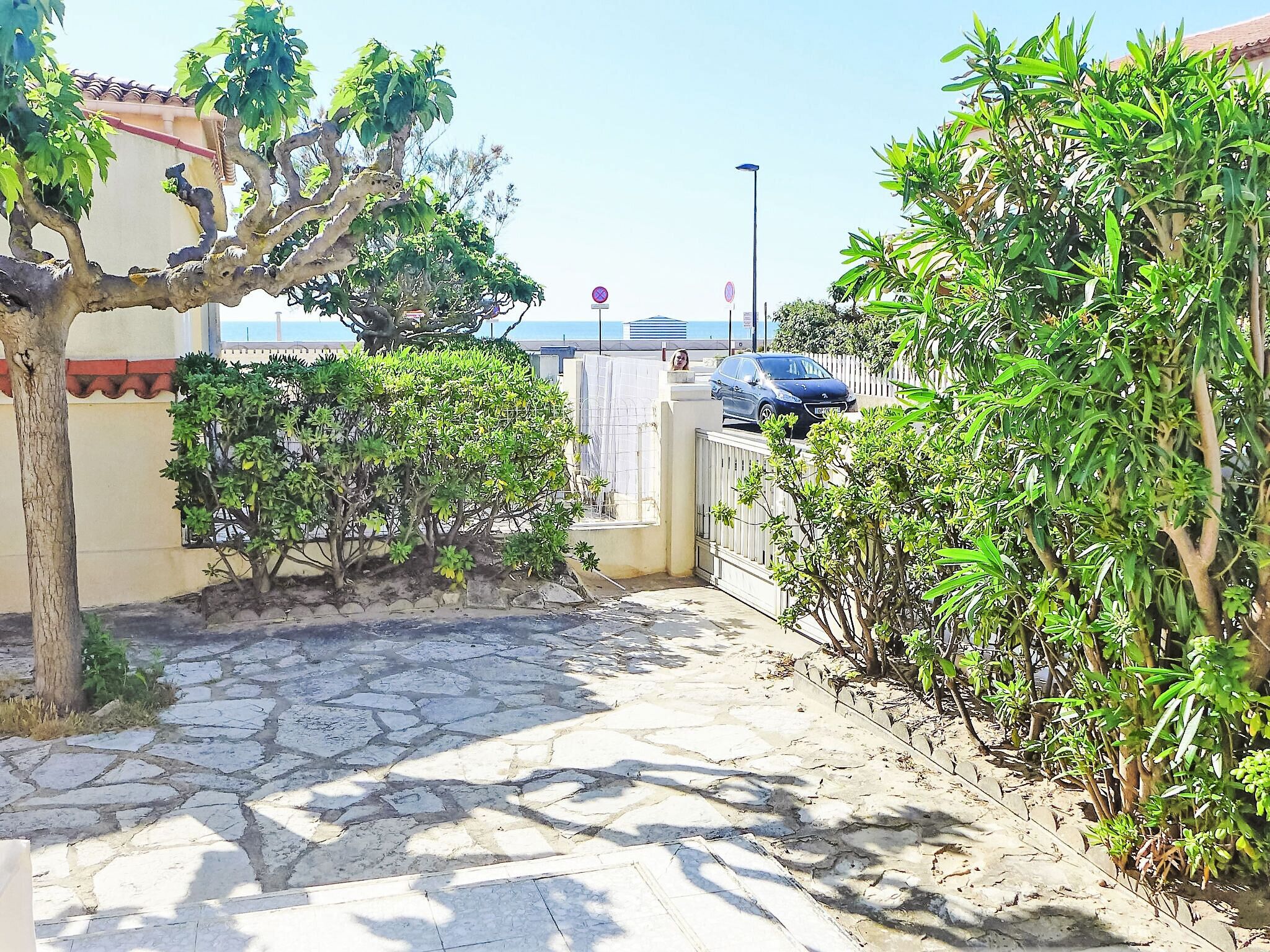 A paved pathway leading to a gated entrance with a blue car parked nearby.