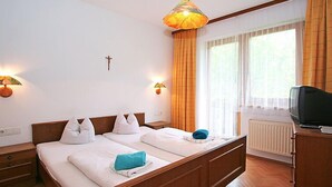 A hotel room with a wooden bed, two bedside lamps, a cross on the wall, and a window with curtains. - Gasteighof by Interhome (Fügen)