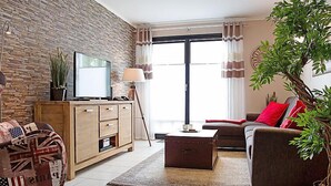 Ein Wohnzimmer mit Steinswand, Fernseher, Sofa, Couchtisch und einer Zimmerpflanze.