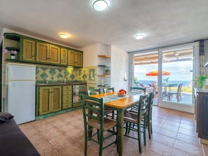 A kitchen with green cabinets, a dining table with chairs, and a view of the ocean through a sliding glass door.