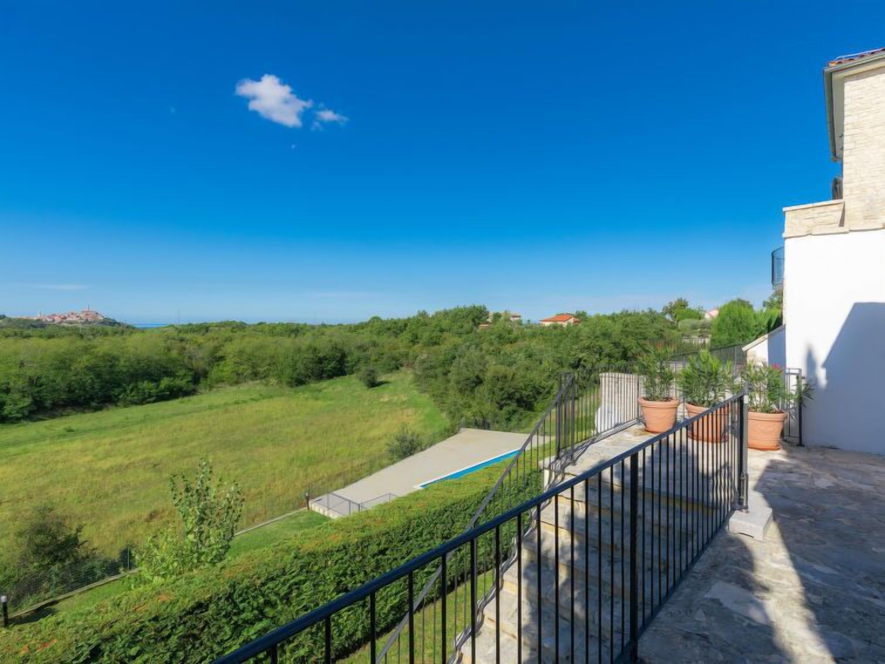 Un balcón con vista a un campo verde y edificios lejanos.