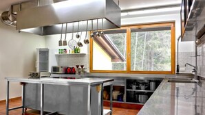A modern kitchen with a large stainless steel island, overhead ventilation, and a window providing natural light.