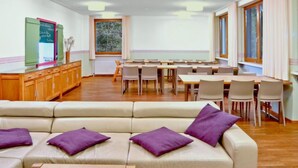A modern dining area with a long table and chairs, a sofa with purple cushions, and a kitchen area with wooden cabinets and a chalkboard.