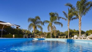 Una piscina azul cristalina rodeada de palmeras y sillas de descanso, con un edificio a un lado.