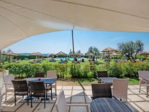 An outdoor patio area with wicker furniture and umbrellas, overlooking a pool and garden.