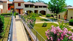 Un barrio residencial con varias casas de dos pisos, un sendero pavimentado y jardines bien cuidados con flores rosadas.