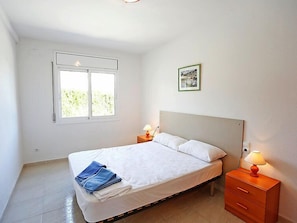 Un dormitorio con una cama, dos mesitas de noche, una ventana y un cuadro enmarcado en la pared.