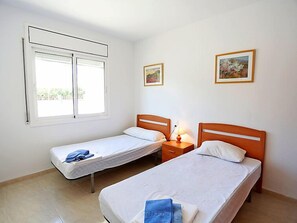 A simple, clean room with two single beds, a window, and two framed pictures on the wall. - Villa Llobeta by Interhome (L'Ametlla de Mar)