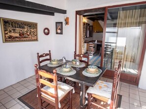 Un coin repas avec une table dressée pour quatre personnes, entourée de chaises en bois. Un tableau et une photographie encadrée ornent le mur.