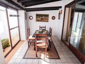 Un coin repas avec une table dressée pour quatre personnes, entourée de chaises en bois. Une grande fenêtre se trouve d’un côté et une porte de l’autre.