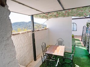 Eine kleine Terrasse im Freien mit Tisch und Stühlen, einer weißen Wand und Blick auf die Berge.