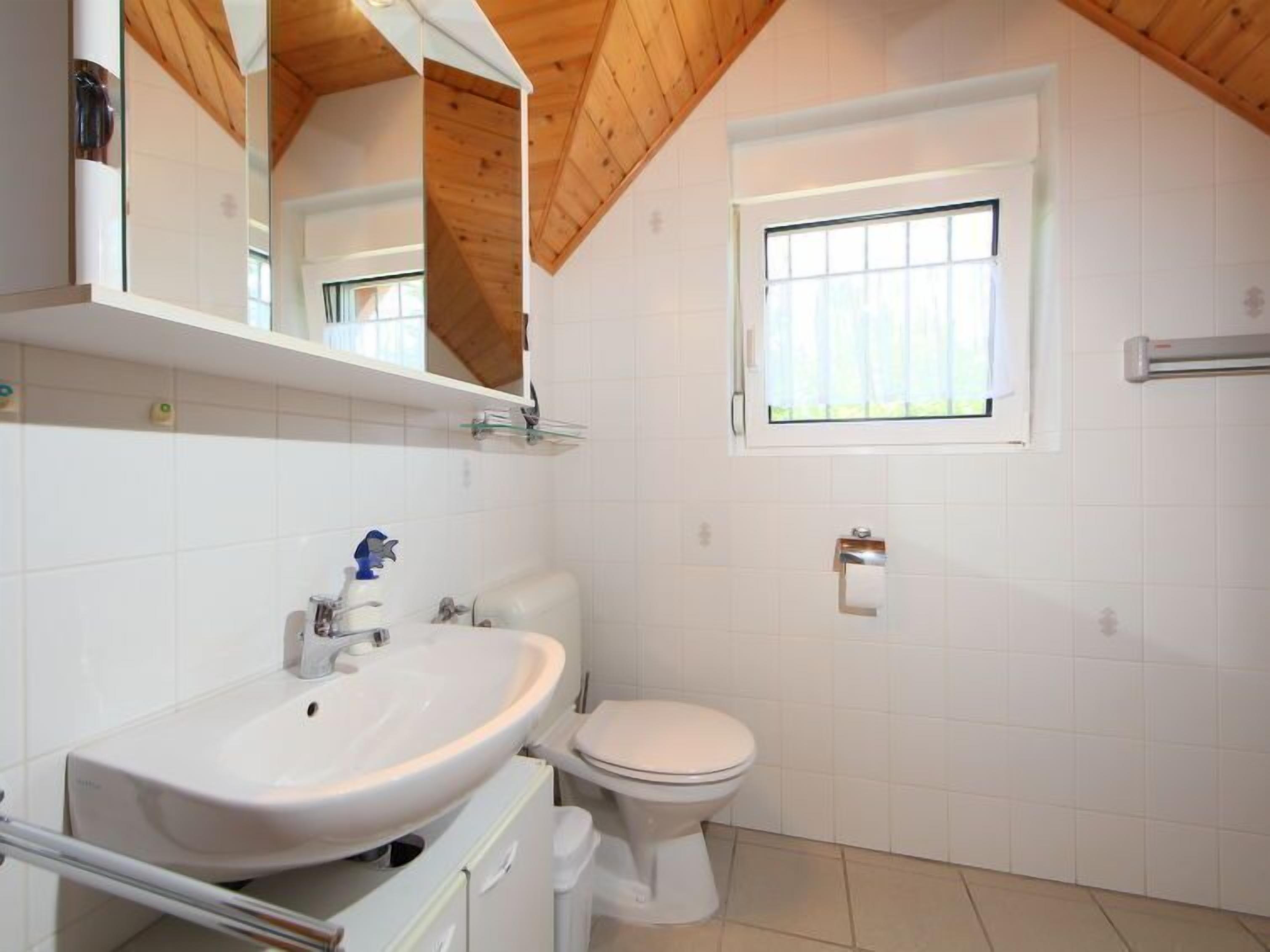 Ein Badezimmer mit einem weißen Waschbecken, einer Toilette und einem Fenster über der Toilette.