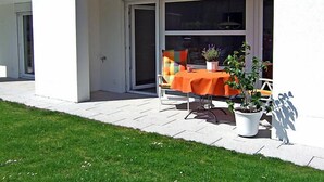 Une terrasse extérieure avec une table et des chaises, une plante en pot et une porte-fenêtre coulissante.