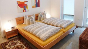 Un lit double avec une literie à rayures, une table de chevet, un tapis et des œuvres d’art abstraites accrochées au mur.