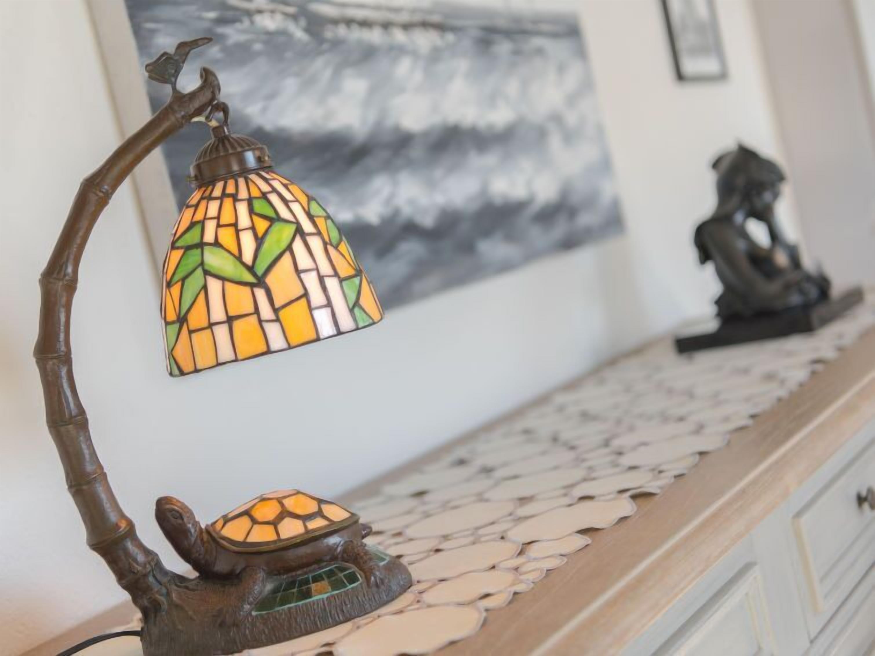Una lámpara decorativa con un diseño de mosaico, una escultura de tortuga y un camino de mesa de mosaico sobre una superficie de madera.