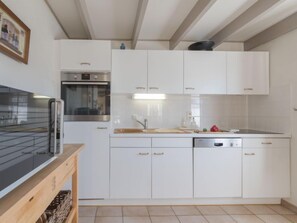 A modern kitchen with white cabinets, a built-in oven, a dishwasher, and a wooden countertop.