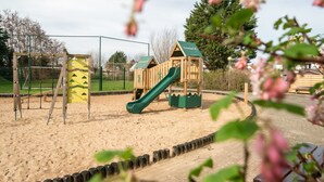 A playground with a slide and climbing structures, surrounded by a fence and sand area. - Vissershuisje 213 with parking by Interhome (Bredene)