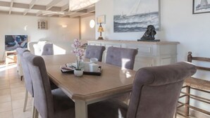 A dining area with a wooden table, six chairs, and a vase with flowers. - Vissershuisje 213 with parking by Interhome (Bredene)