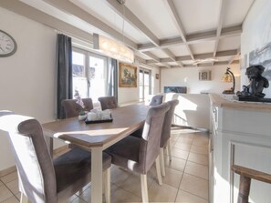 A dining area with a wooden table and chairs, a clock on the wall, and a window with curtains.