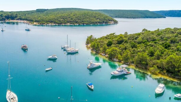 Un port de plaisance où sont amarrés plusieurs bateaux, entouré de collines verdoyantes et bordé d’une eau d’un bleu limpide.