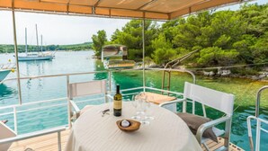 Un espace extérieur abrité, aménagé pour les repas, avec une table pour deux personnes, offrant une vue sur une étendue d’eau où l’on peut apercevoir des bateaux et de la végétation.