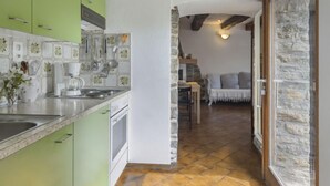 Une cuisine avec des meubles de couleur verte, un mur recouvert de carreaux et un mur en pierre.