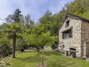 Un bâtiment en pierre à l’aspect rustique, entouré d’une végétation luxuriante et d’arbres.