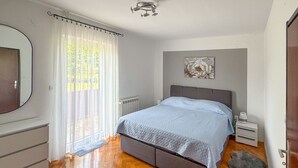 A bedroom with a bed, a bedside table, a nightstand, a radiator, a mirror, and a window with curtains. - Cvjetko by Interhome (Pula/Rakalj)