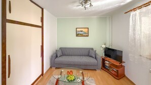 A living room with a grey sofa, a glass coffee table with decorative items, a television on a wooden stand, and a painting on the wall. - Cvjetko by Interhome (Pula/Rakalj)