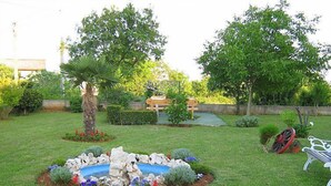 A well-maintained garden with a central rock feature surrounded by colorful flowers, a palm tree, and a bench. - Cvjetko by Interhome (Pula/Rakalj)