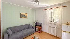 A living room with a grey sofa, a glass coffee table with decorative items, a television on a stand, and a window with curtains. - Cvjetko by Interhome (Pula/Rakalj)