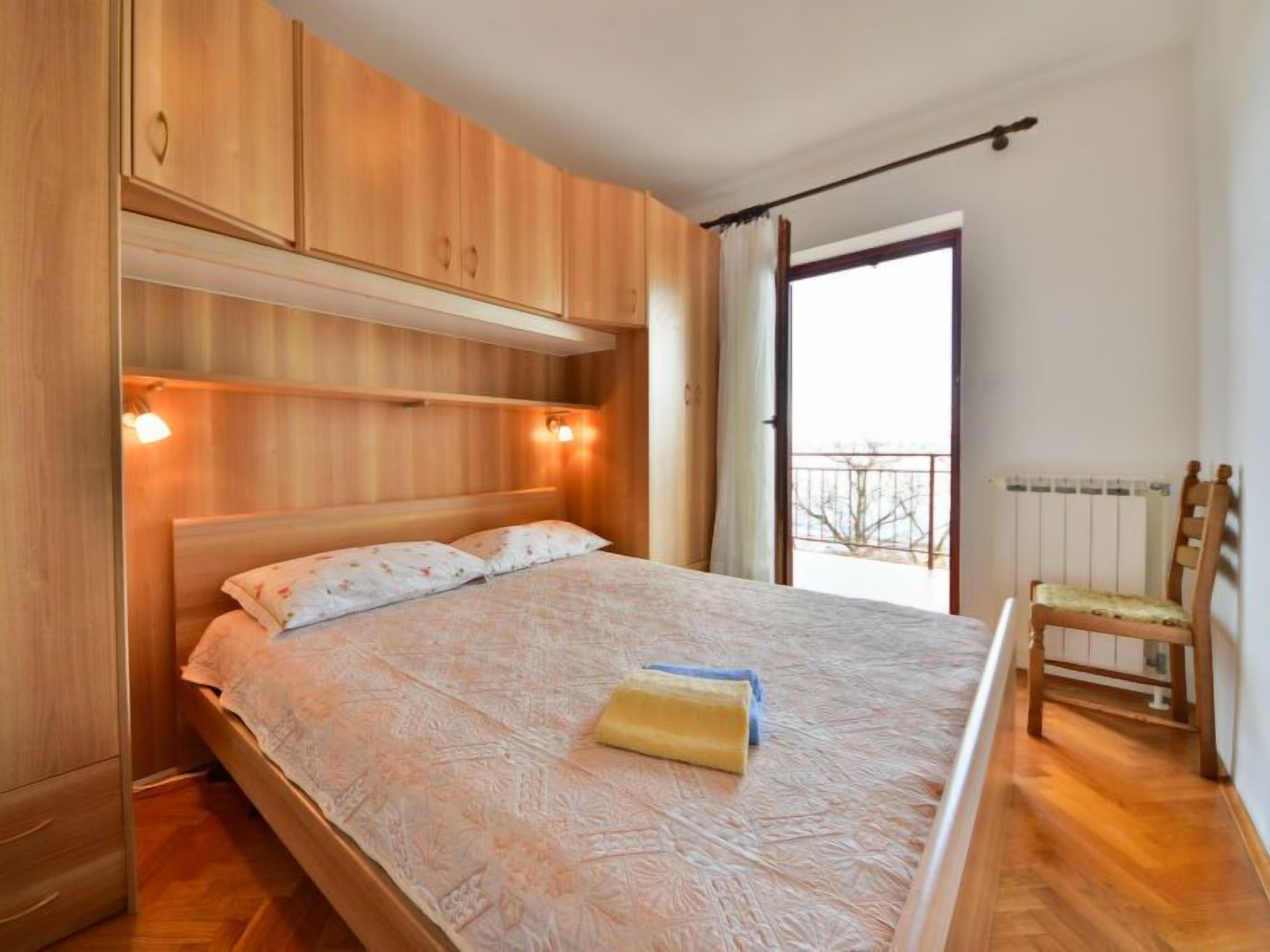 Quarto com cama de madeira, mesa de cabeceira, cadeira e janela com vista.