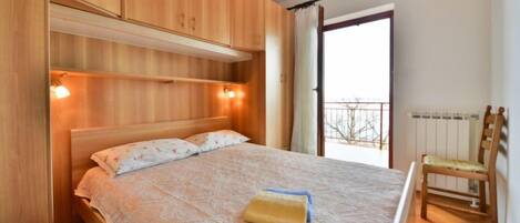 Quarto com cama de madeira, mesa de cabeceira, cadeira e janela com vista.