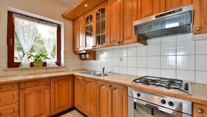A kitchen with wooden cabinets, a gas stove, a sink, and a window with curtains.
