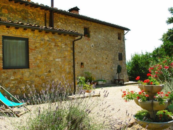 A stone building with a tiled roof, a window, and a garden with lavender and red flowers.