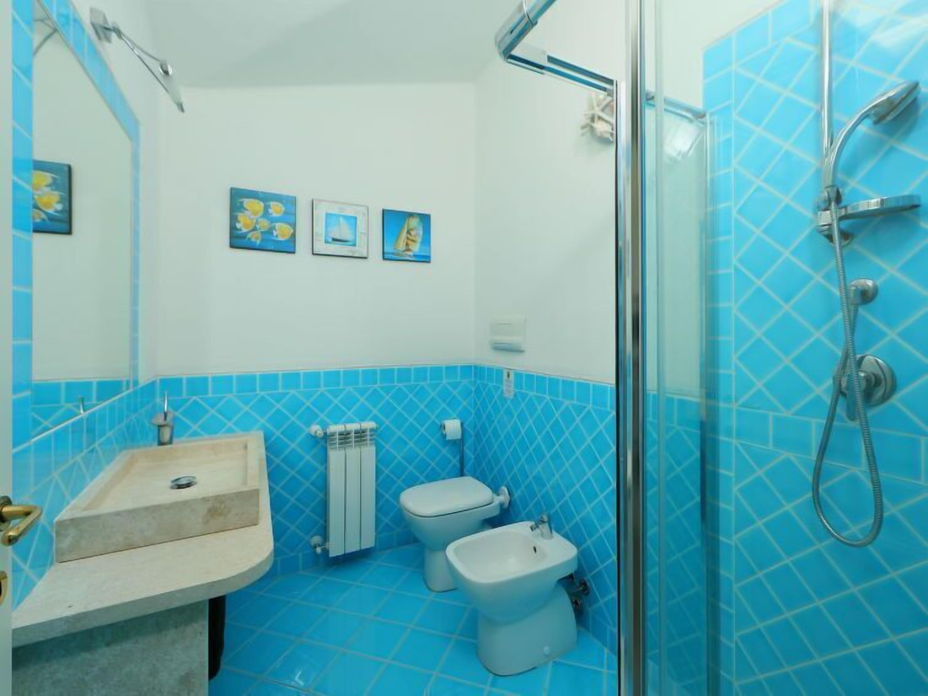 A bathroom with blue tiles, a sink, a toilet, a bidet, and a glass shower enclosure.