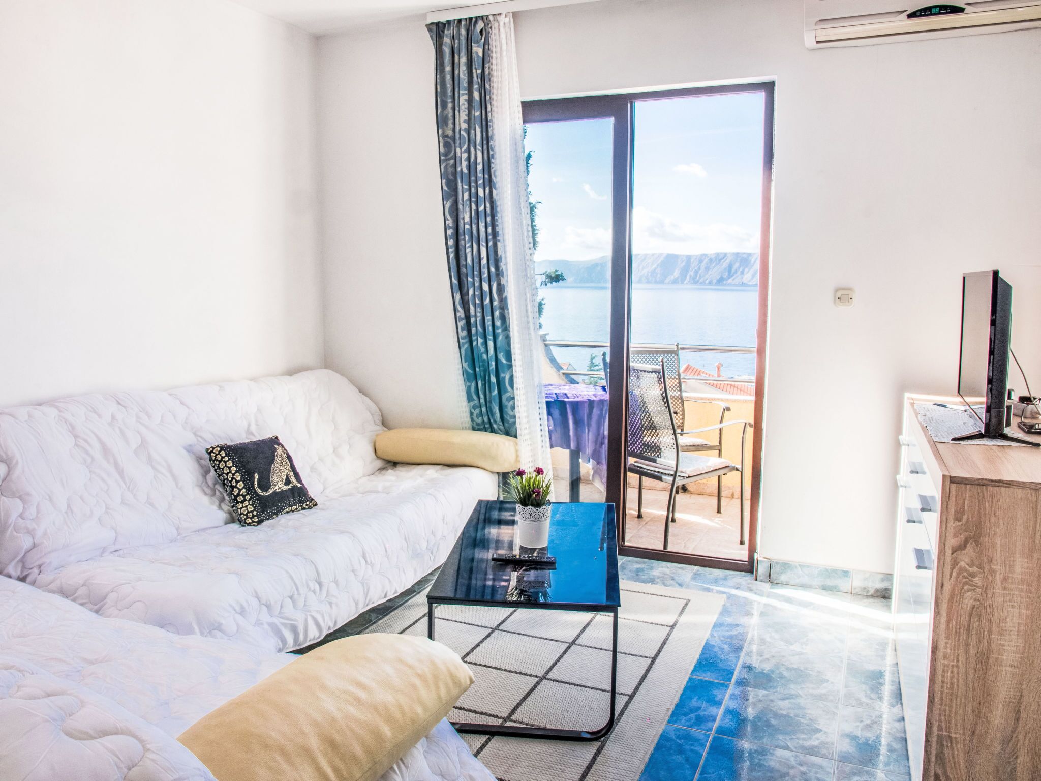 A modern room with a white sofa, a small coffee table, and a view of the sea through a glass door.