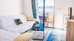 Une pièce moderne avec un canapé blanc, une petite table basse et une vue sur la mer, visible à travers une porte vitrée.
