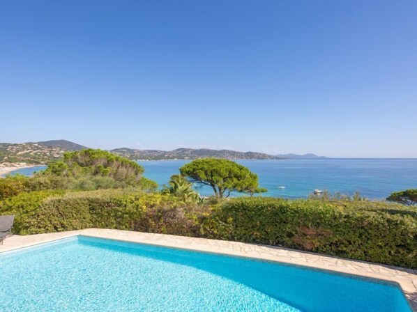 Piscina com vista para o mar e colinas ao longe.