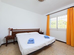 Een slaapkamer met een houten bed, een nachtkastje, een lamp en een raam met gordijnen.