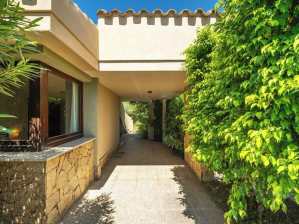 A narrow pathway leading to a building with a stone wall on one side and a green hedge on the other.