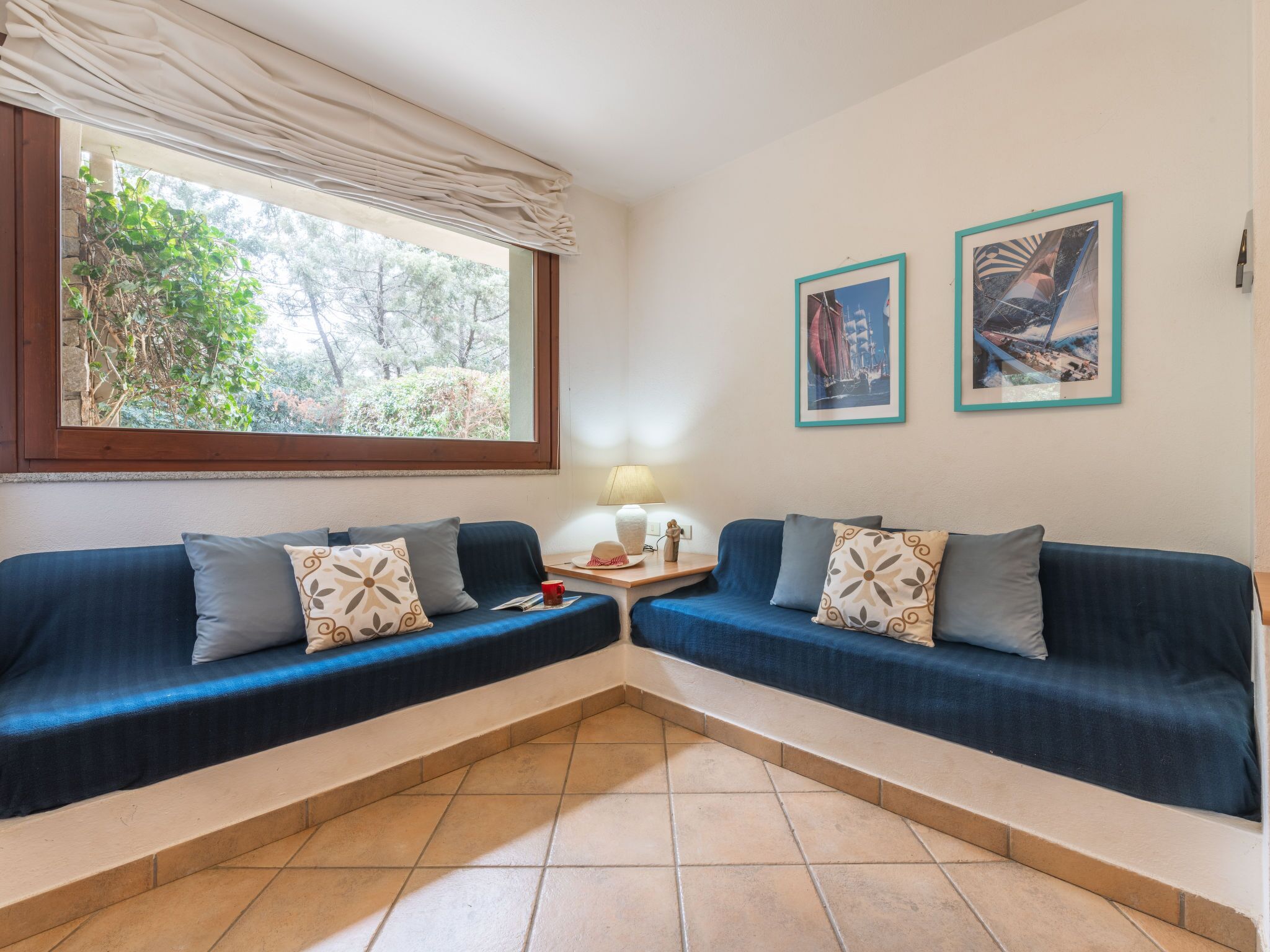 A room with two blue sofas, a small table with a lamp, and two framed pictures on the wall.