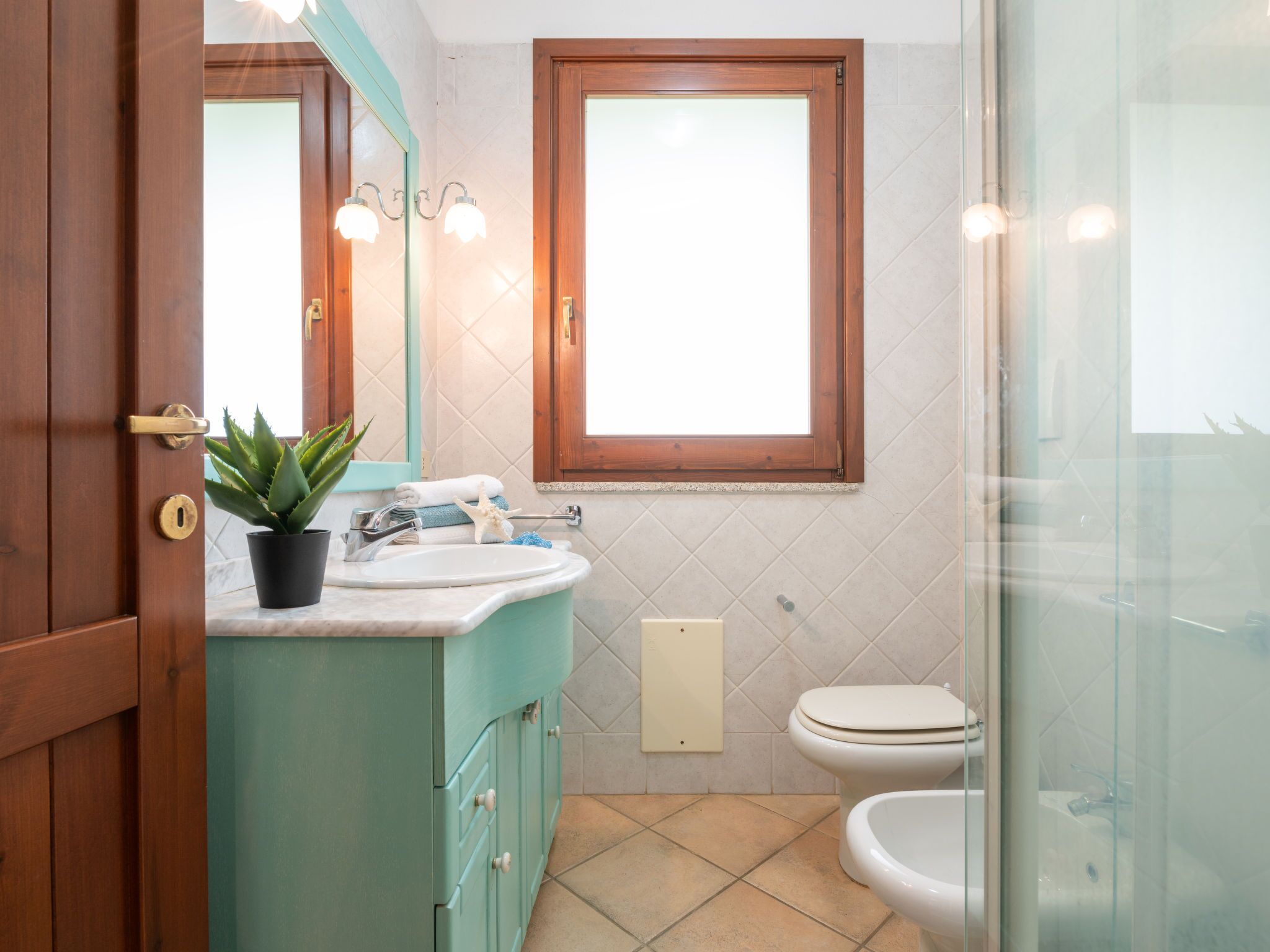 Un baño con puerta de madera, un lavabo con espejo, una ventana y un inodoro.