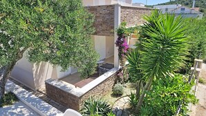 Un immeuble résidentiel doté d’une façade en pierre, d’un balcon orné d’une balustrade en pierre et d’un jardin où poussent diverses plantes, dont un palmier.