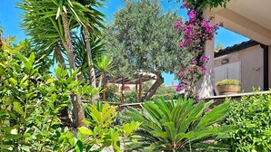Un jardin avec différentes espèces de plantes, une pergola et un bâtiment à la façade blanche.