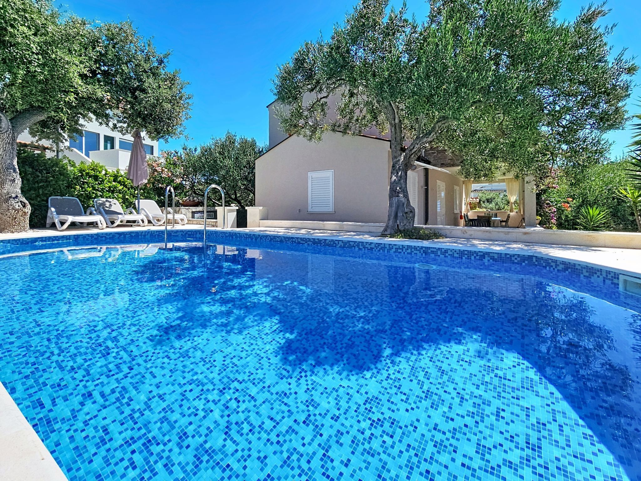 Una piscina con acqua cristallina, circondata da sdraio e alberi.