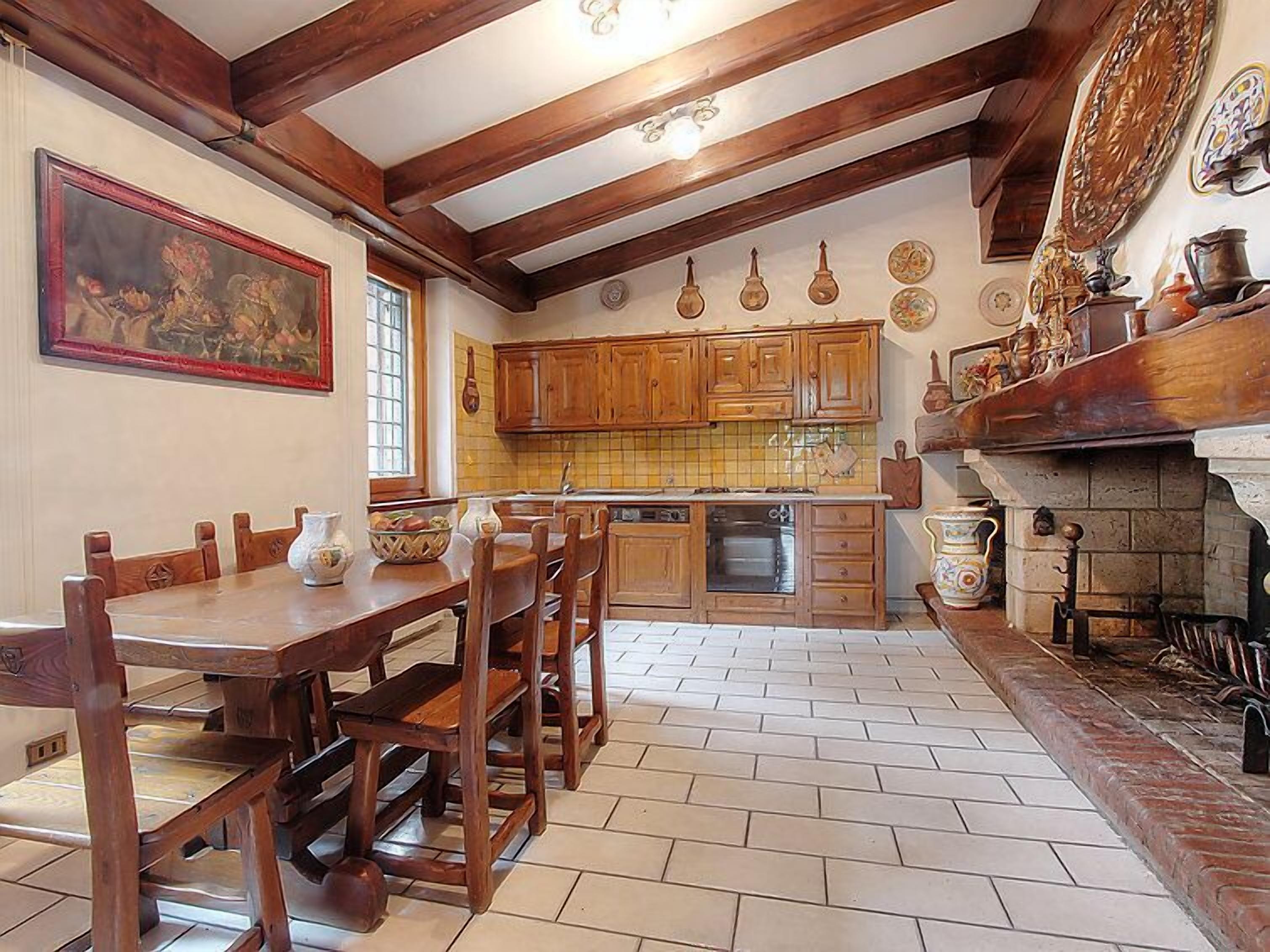 Een traditionele keuken met houten kastjes, een betegelde spatwand en een open haard van baksteen.