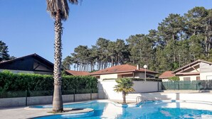 A swimming pool with a palm tree, surrounded by a fence, and houses in the background. - Bosquet aux Ecureuils by Interhome (Capbreton)