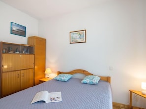 Een slaapkamer met een bed, een nachtkastje met een lamp, een kledingkast en twee ingelijste foto's aan de muur.