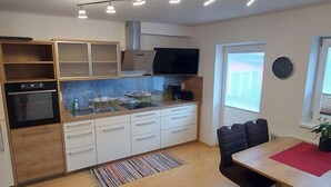 A modern kitchen with a built-in oven, a microwave, and a coffee machine. There is a dining area with a table and chairs. - Rupertus by Interhome (Zell am See)